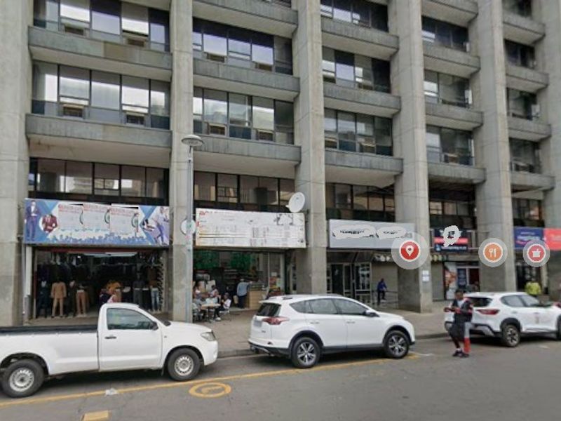 Street-level view of a multi-story commercial building featuring concrete structural elements and multiple ground-floor retail storefronts.