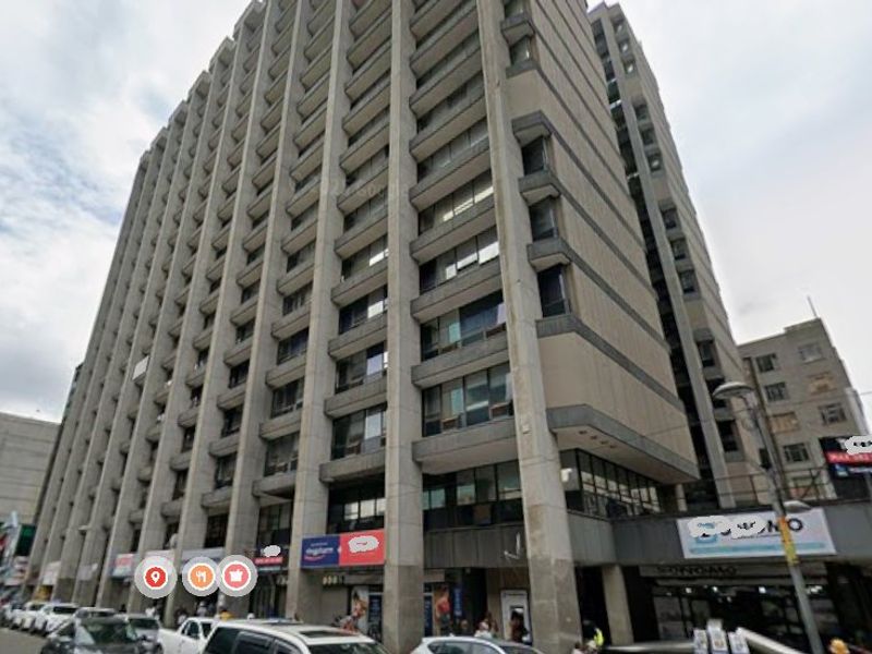 A multi-story commercial high-rise building featuring a concrete facade and ground-level retail storefronts in an urban setting.