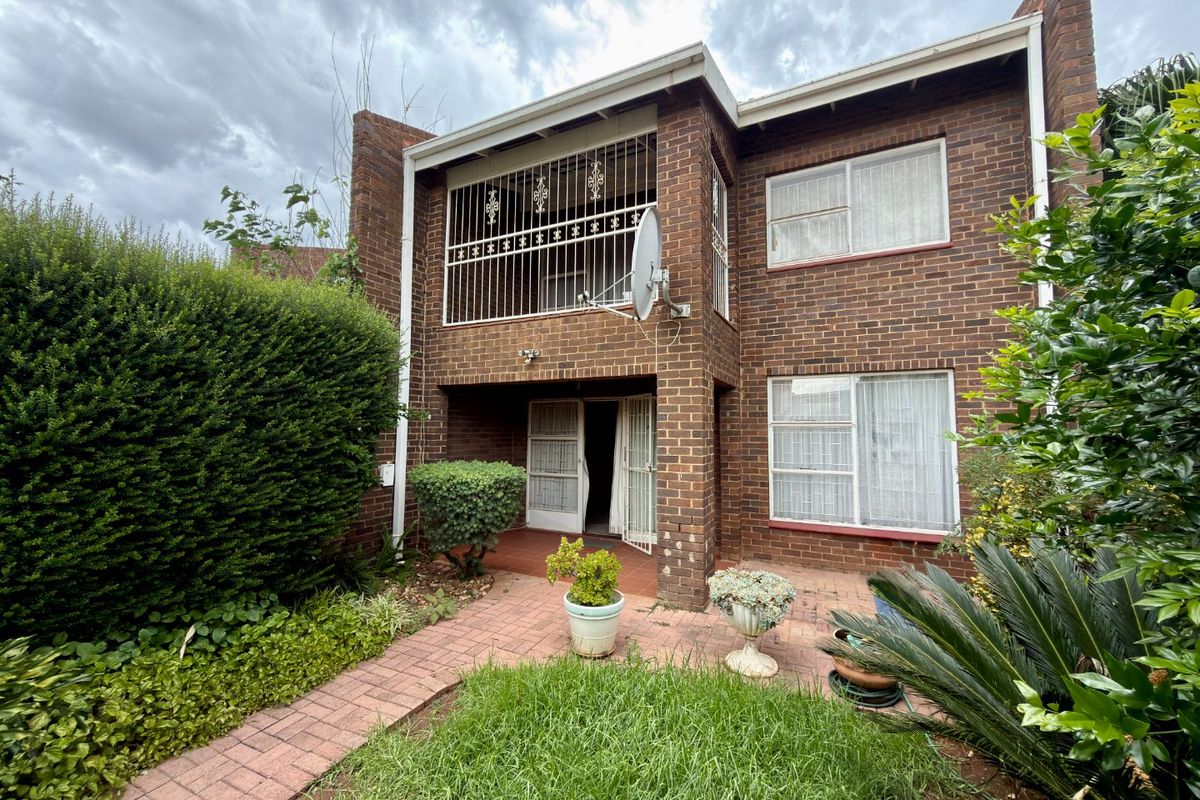 Rear view of a double-story brick townhouse featuring a paved patio area, established garden, and security bars on the upper balcony.