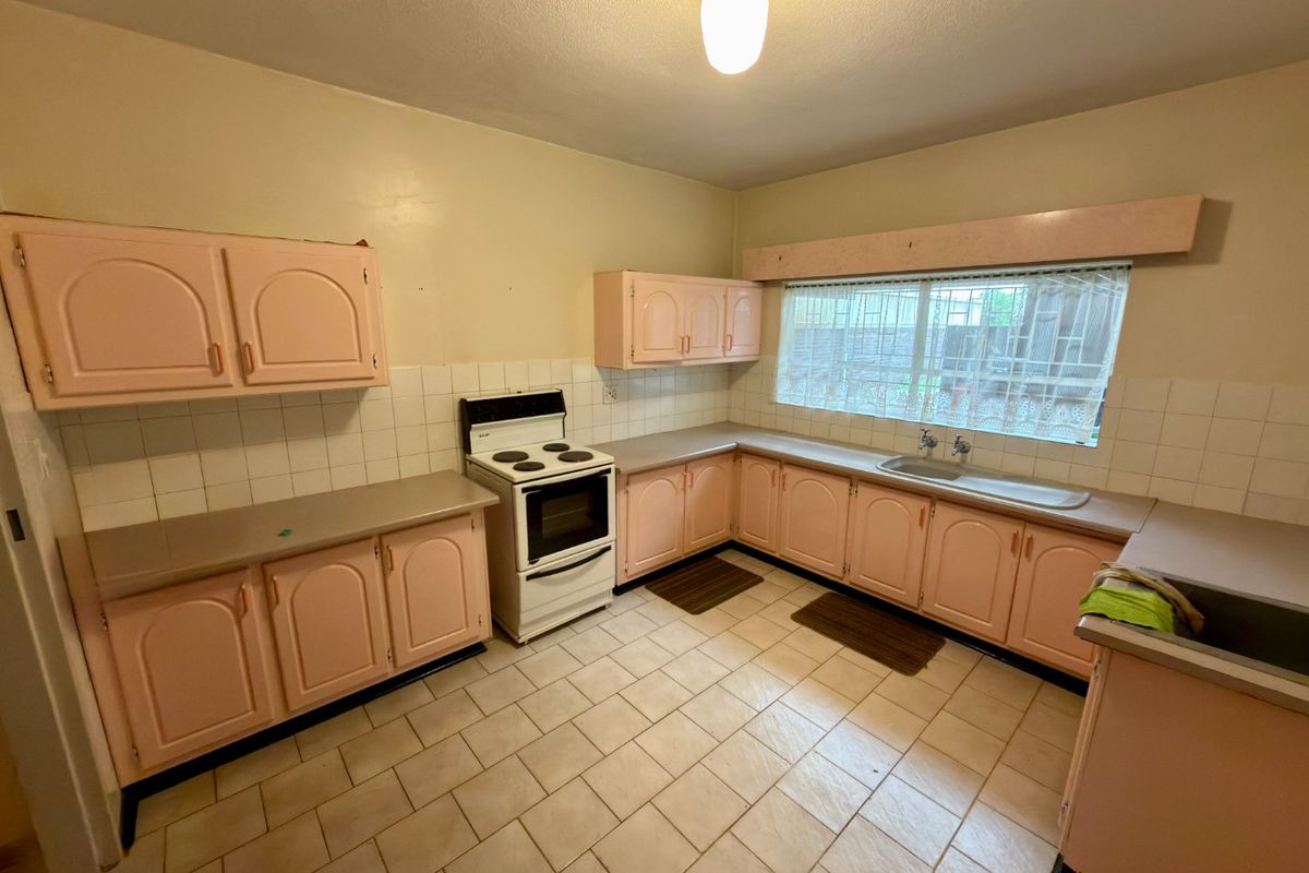 A dated kitchen featuring original pink cabinetry, tiled countertops, and ceramic floor tiles, offering a functional layout ready for modern renovation.