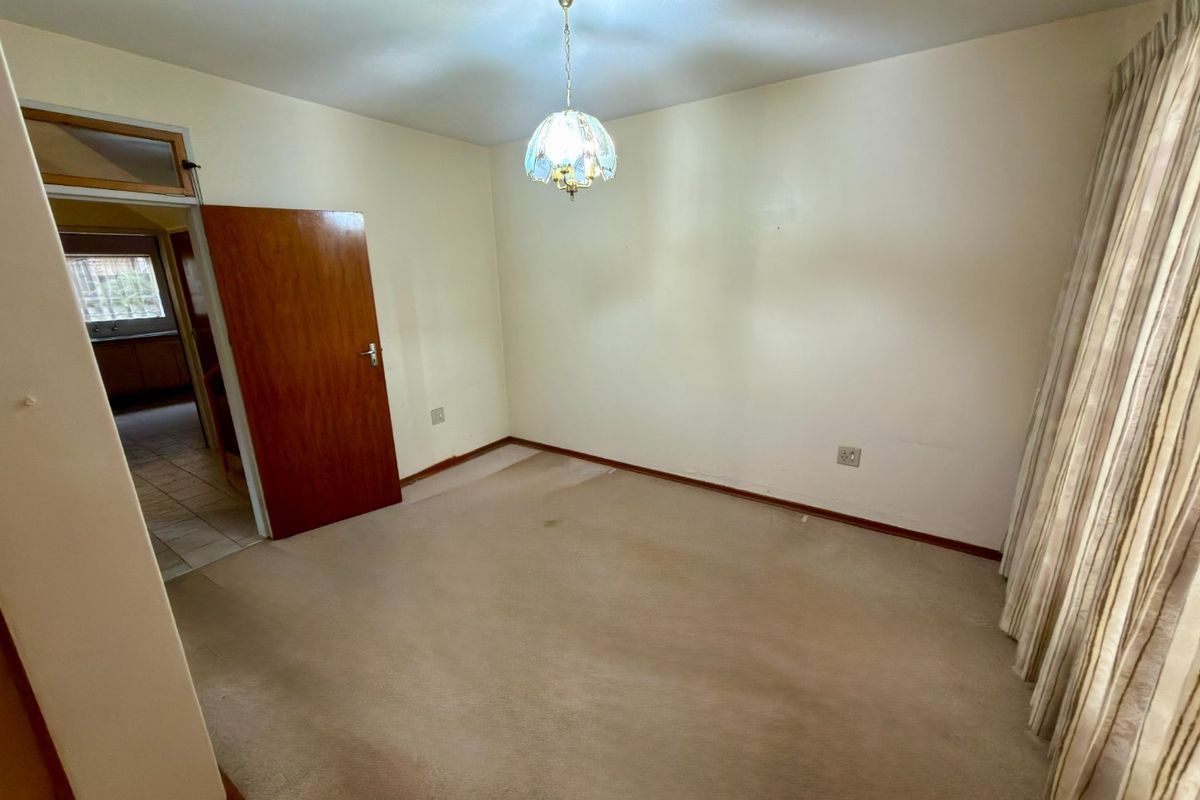 A vacant bedroom featuring neutral wall finishes, carpeted flooring, and a central pendant light fixture, with an adjacent view into a tiled hallway.