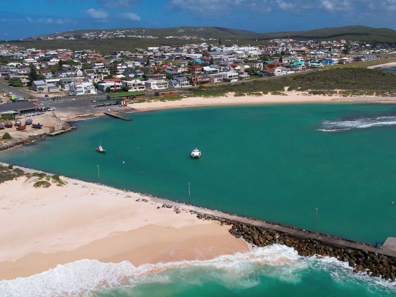 Aerial view of the coastal town, sandy beach, and stone jetty extending into the turquoise ocean.