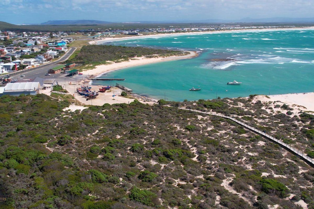 An aerial view of the coastal landscape, featuring a boardwalk, harbour area, and proximity to the beach and residential neighbourhood.