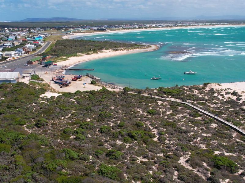 An aerial view of the coastal landscape, featuring a boardwalk, harbour area, and proximity to the beach and residential neighbourhood.