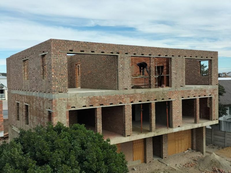 A multi-story apartment building under construction, featuring exposed brickwork and structural concrete framing in an early development phase.