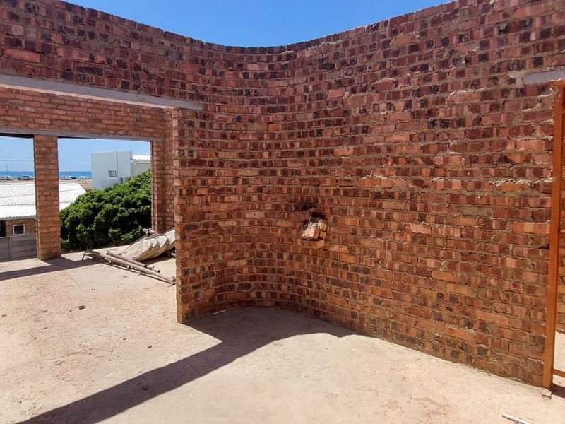 An unfinished open-plan interior space featuring exposed brick walls and concrete flooring, currently in a shell construction state.