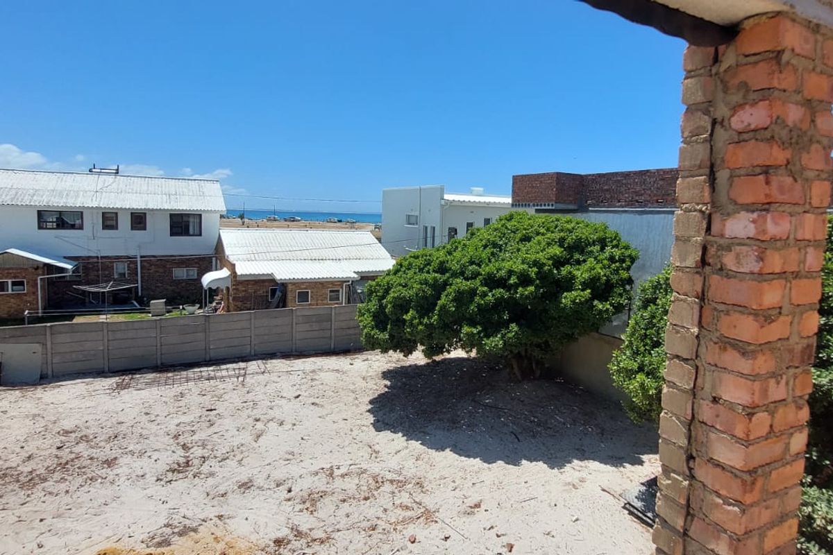 Rear exterior view showing a sandy yard, precast boundary wall, and a brick pillar with visible structural cracking.