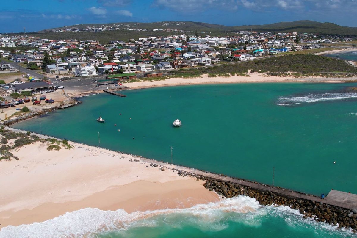 Aerial view of the coastal town, sandy beach, and jetty extending into the turquoise ocean.