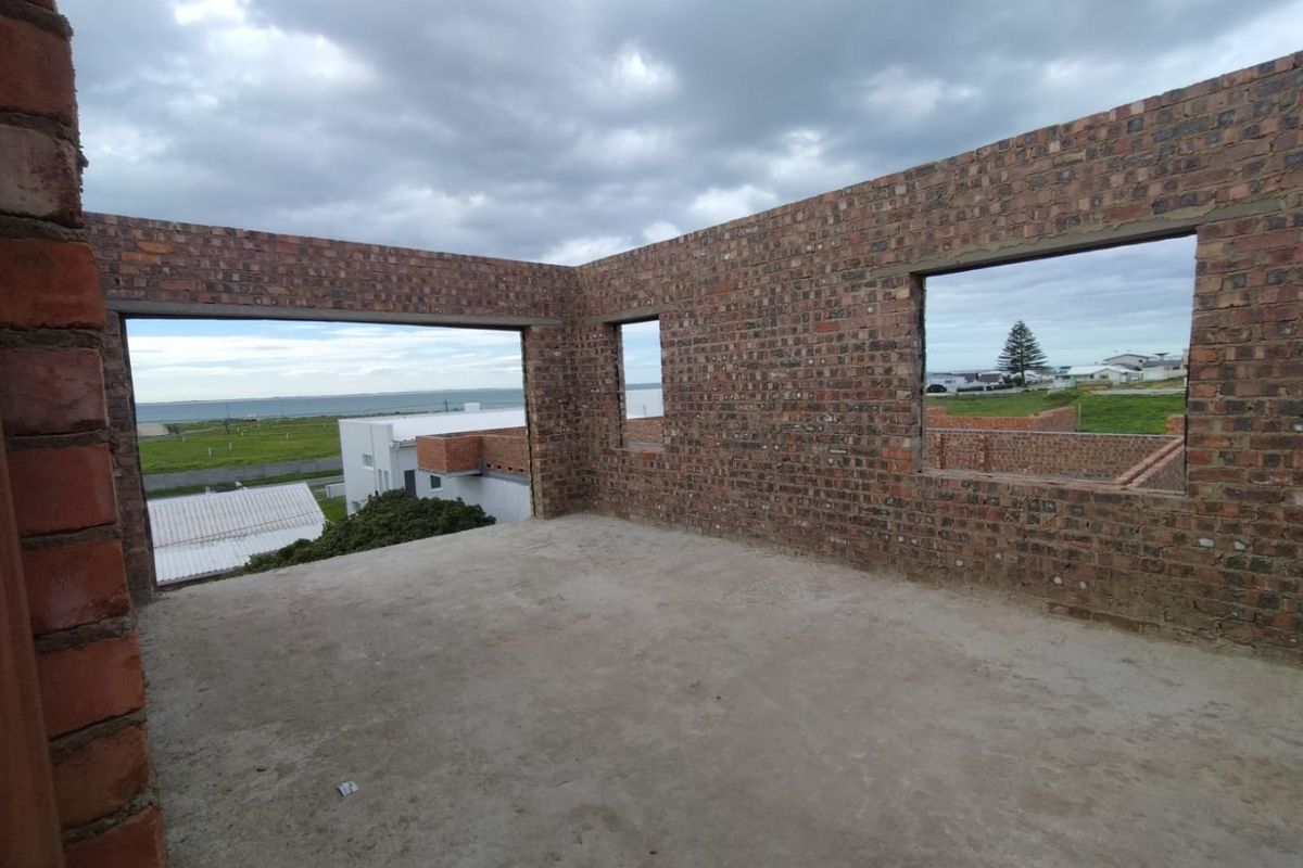 An unfinished interior space under construction featuring exposed brick walls and a concrete floor slab with open window frames overlooking the coastal area.