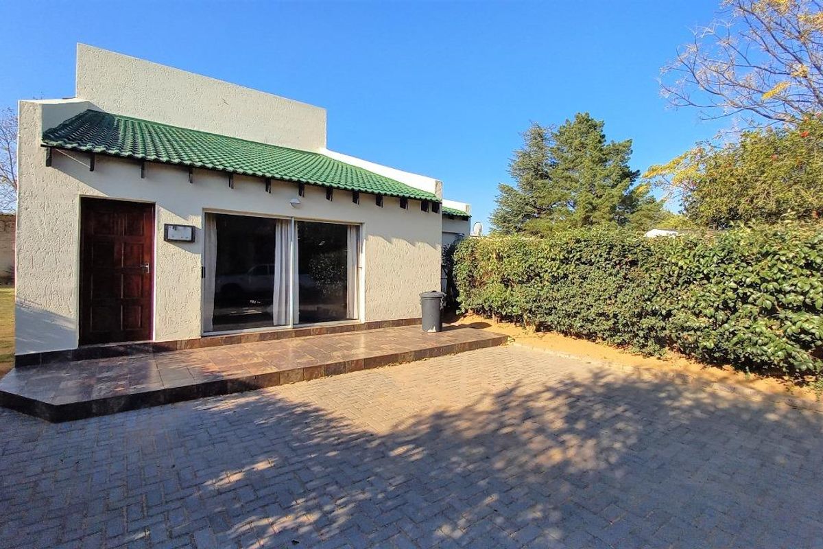 Rear view of the property featuring a paved patio area, sliding glass doors, and a well-maintained hedge boundary.