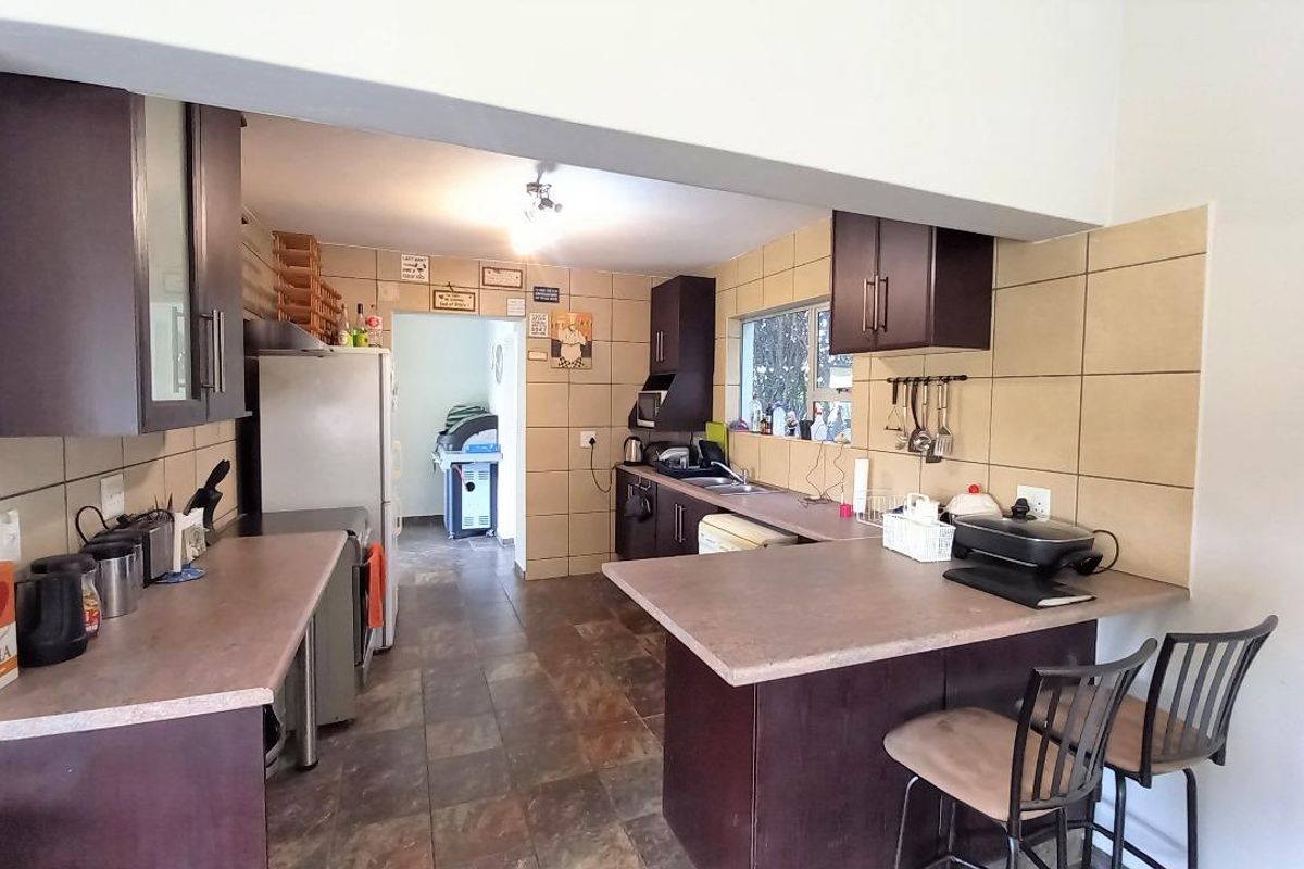 Functional kitchen featuring dark cabinetry, laminate countertops, tiled backsplash, and a breakfast bar, with an adjacent scullery area.