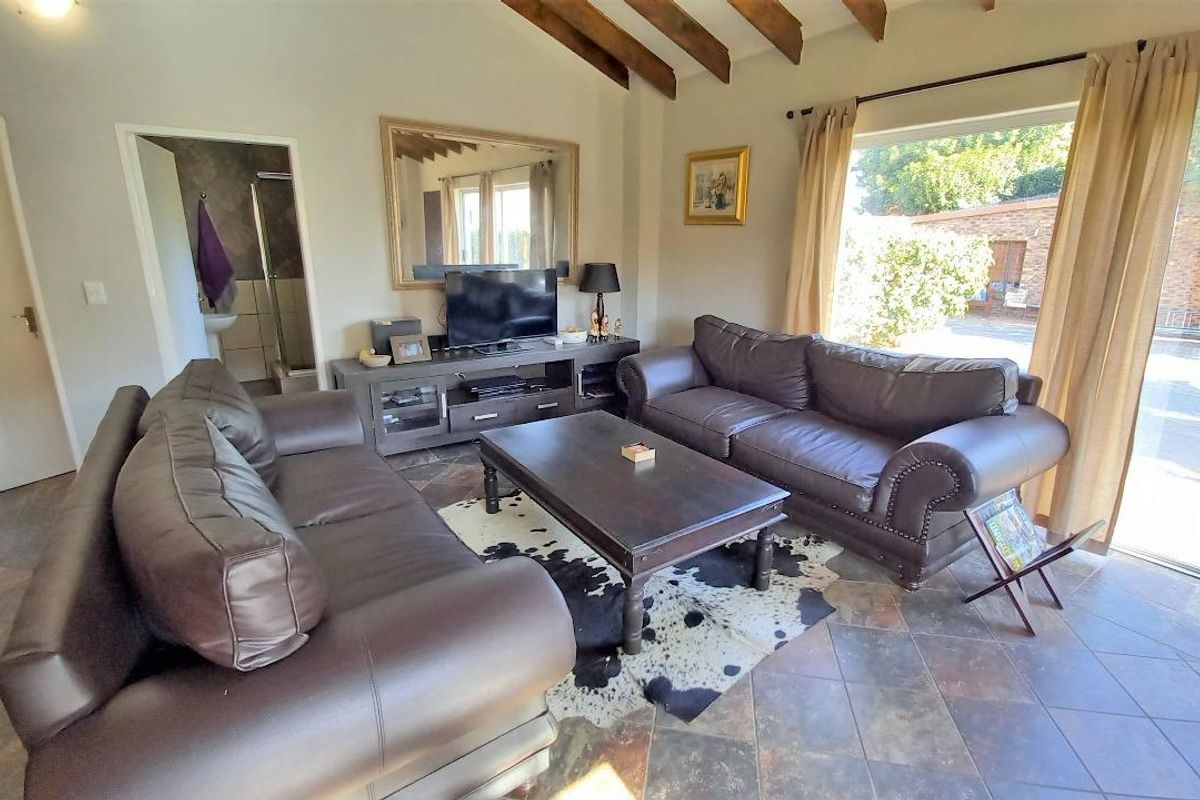 Spacious living room featuring exposed timber ceiling beams, slate tile flooring, and large sliding glass doors providing natural light and garden access.