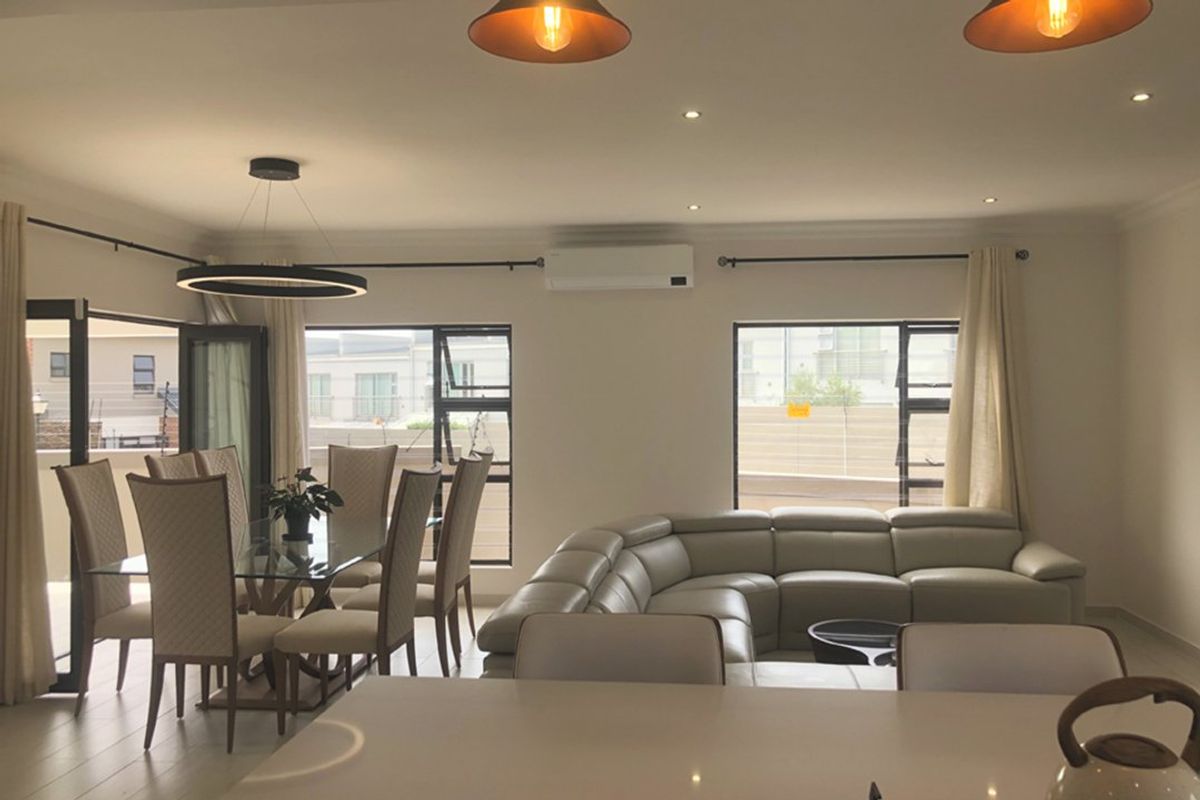 Spacious open-plan living and dining area featuring tiled floors, modern lighting, and a wall-mounted air conditioning unit with large windows for natural light.