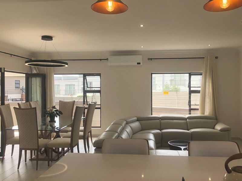 Spacious open-plan living and dining area featuring tiled floors, modern lighting, and a wall-mounted air conditioning unit with large windows for natural light.