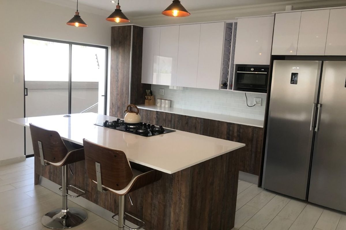 Modern kitchen featuring a central island with a gas hob, sleek cabinetry, subway tile backsplash, and integrated appliances, opening to an outdoor area.