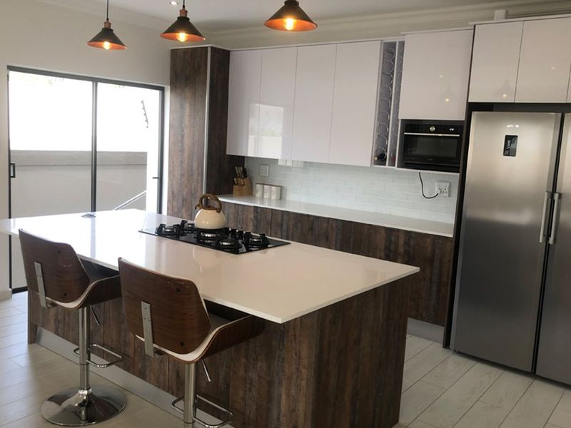 Modern kitchen featuring a central island with a gas hob, sleek cabinetry, subway tile backsplash, and integrated appliances, opening to an outdoor area.