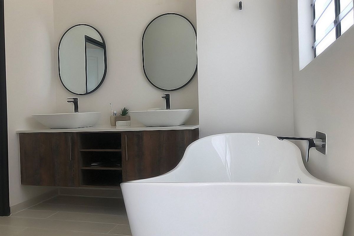 Modern bathroom featuring a double vanity with vessel sinks, oval mirrors, and a sleek freestanding bathtub with wall-mounted fixtures.