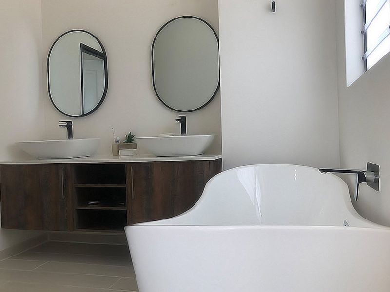Modern bathroom featuring a double vanity with vessel sinks, oval mirrors, and a sleek freestanding bathtub with wall-mounted fixtures.