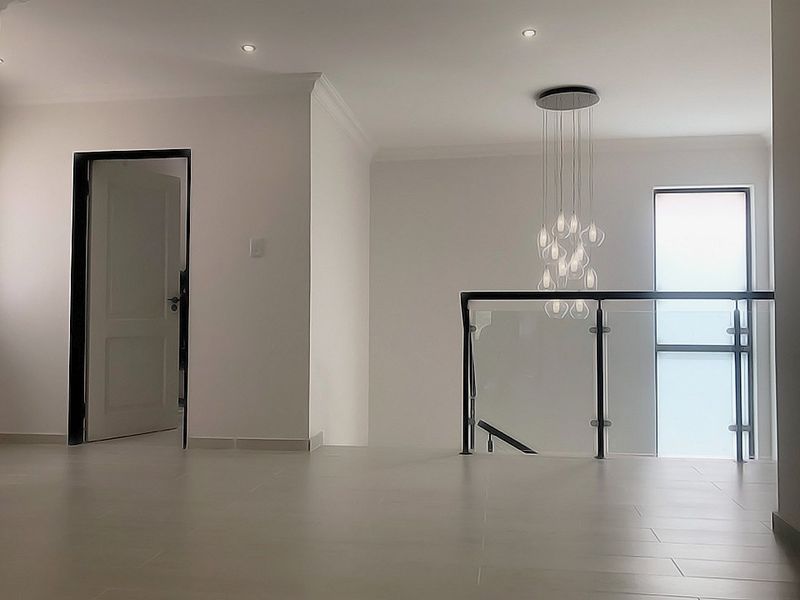 A bright, modern landing area featuring tiled flooring, a glass balustrade, and a contemporary pendant light fixture.