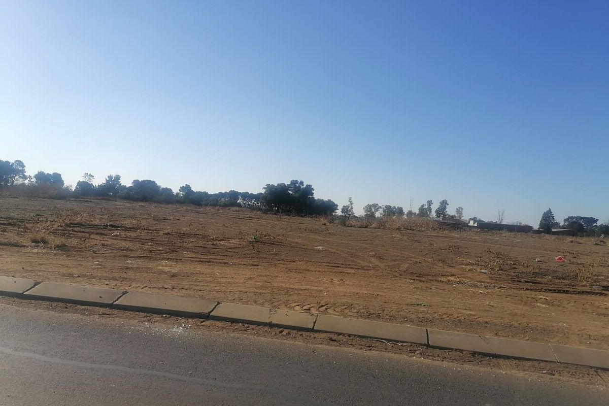 A vacant residential plot of land featuring level terrain, accessible from an adjacent asphalt road with established concrete kerbing.