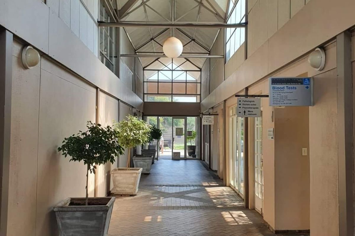 A bright, spacious commercial hallway featuring brick flooring, a high vaulted ceiling with integrated skylights, and clear directional signage for medical facilities.