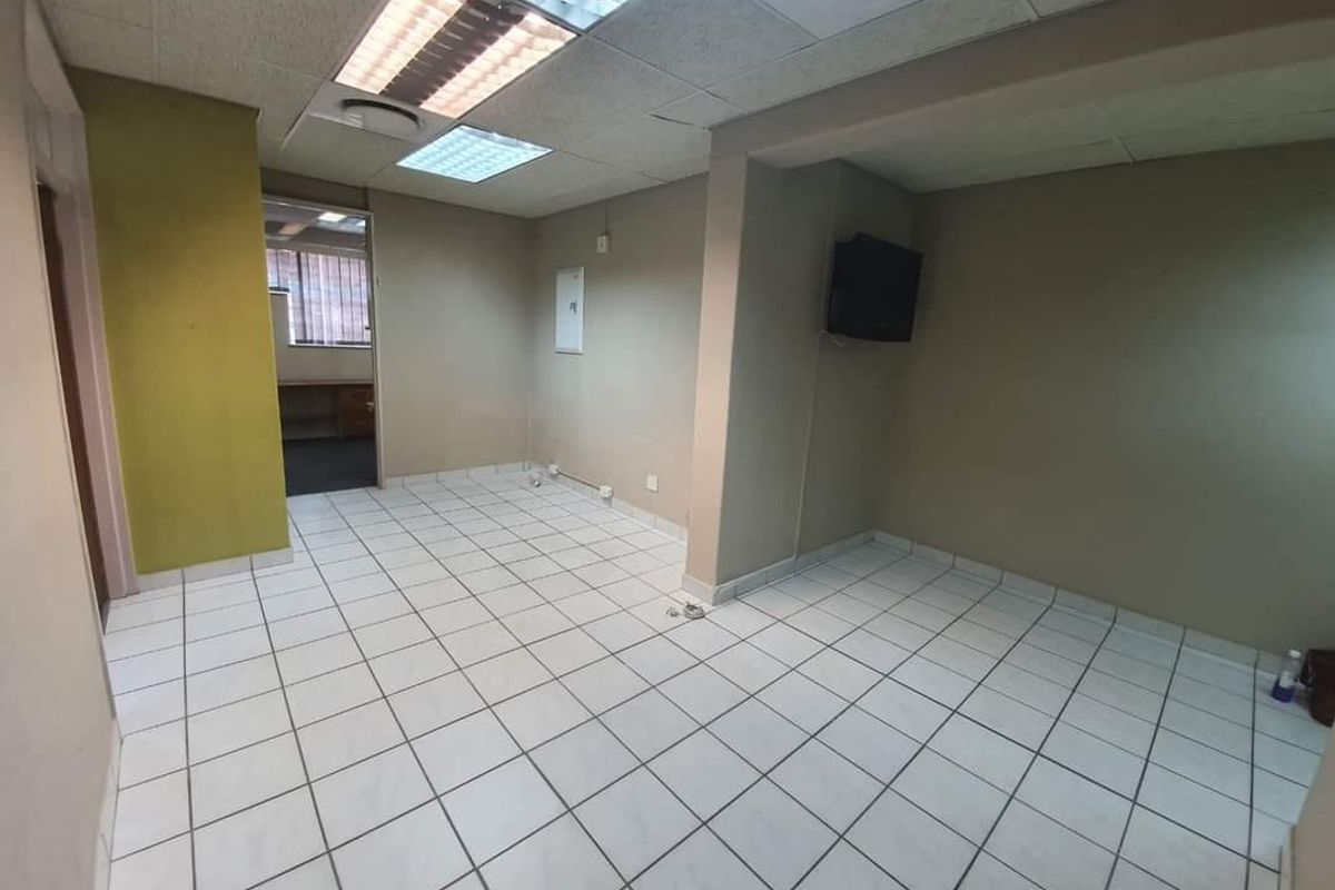An empty commercial office space featuring ceramic tiled flooring, a suspended ceiling with integrated lighting, and neutral wall finishes.