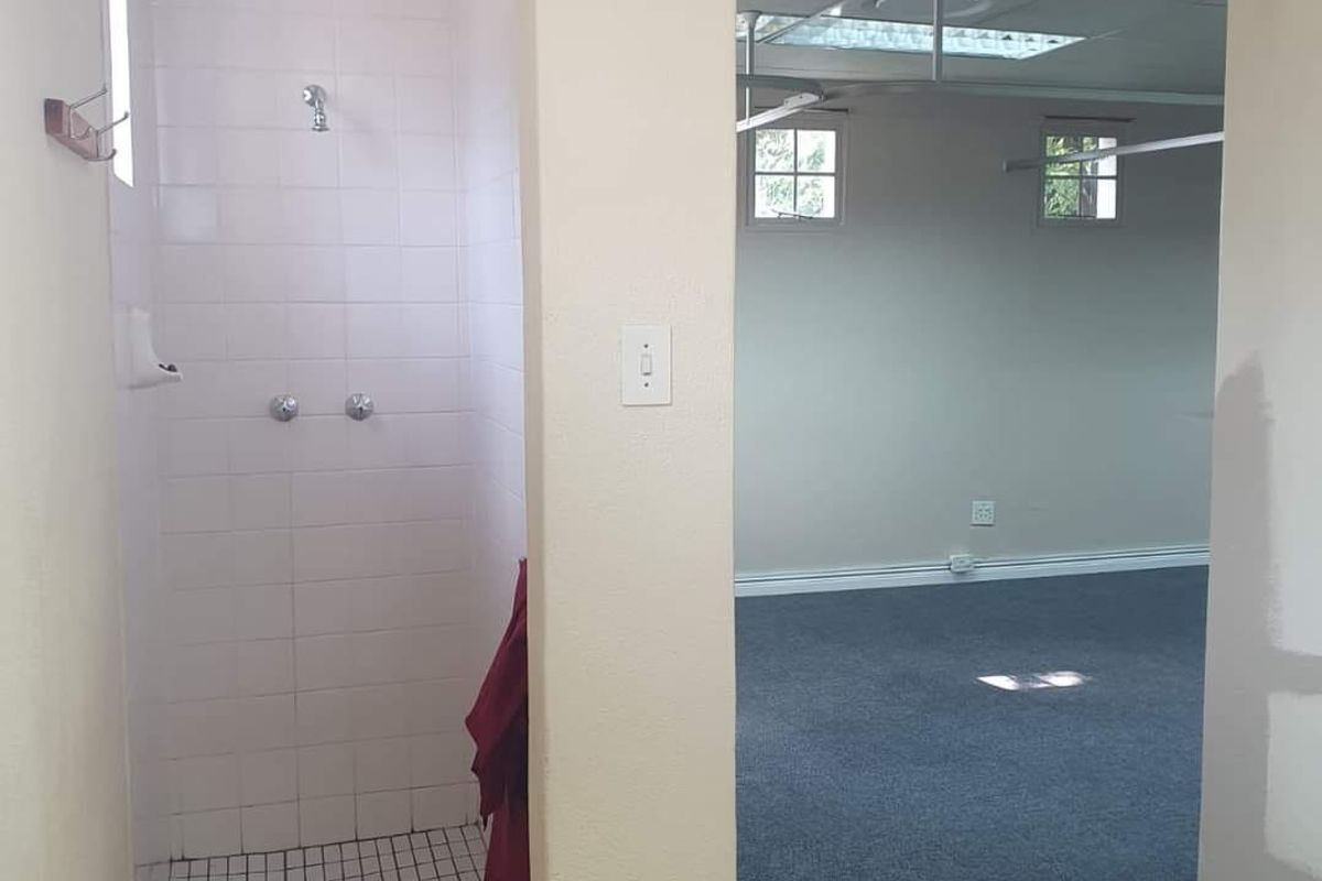 A functional bathroom area featuring a tiled shower cubicle, adjacent to an open-plan office space with carpeted flooring and a suspended ceiling.