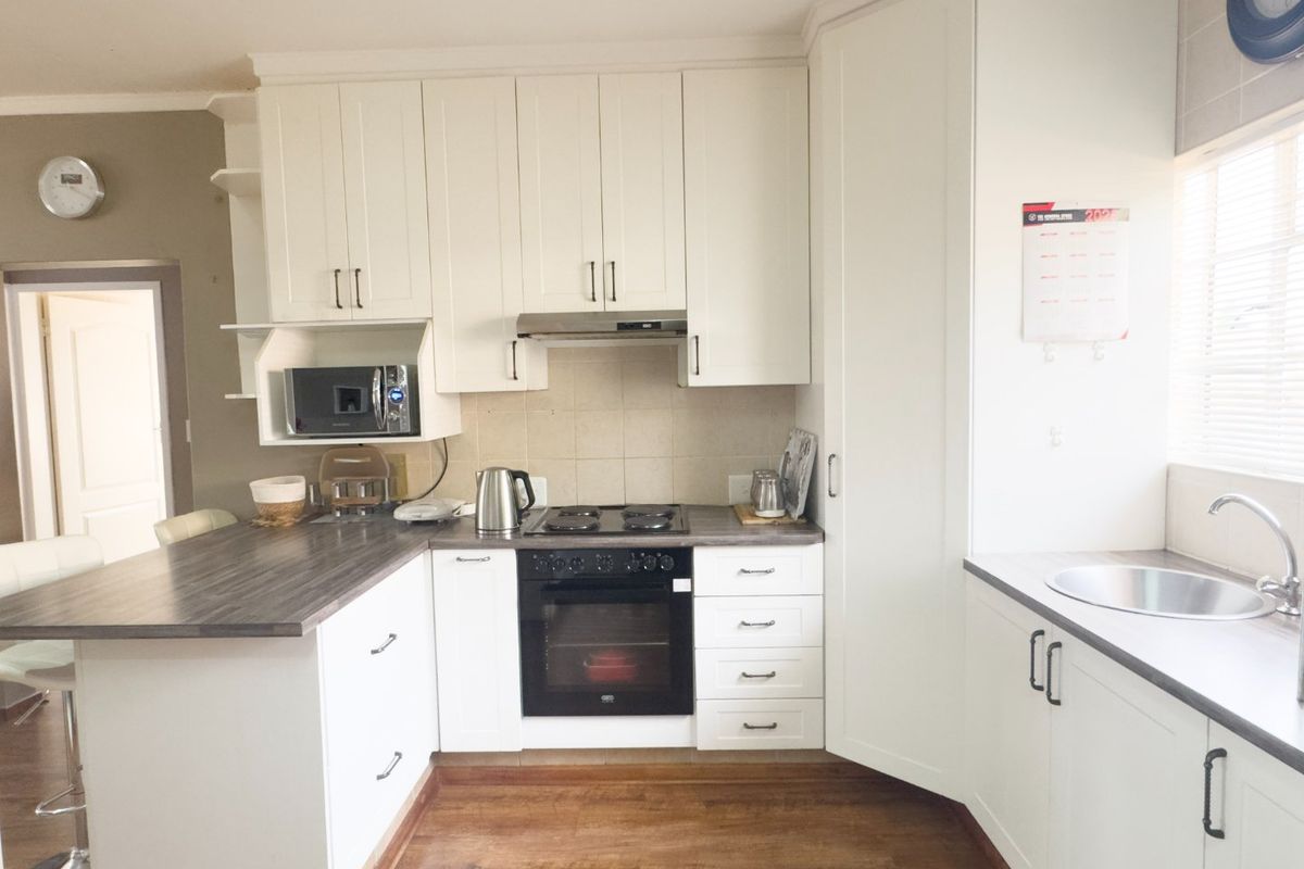A well-maintained kitchen featuring white cabinetry, dark laminate countertops, built-in oven with gas hob, extractor fan, and a stainless steel sink.