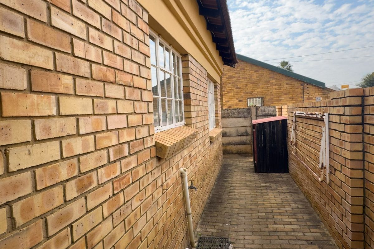 A side exterior walkway featuring face brick walls, paved flooring, and an external water tap, leading towards the rear of the townhouse property.