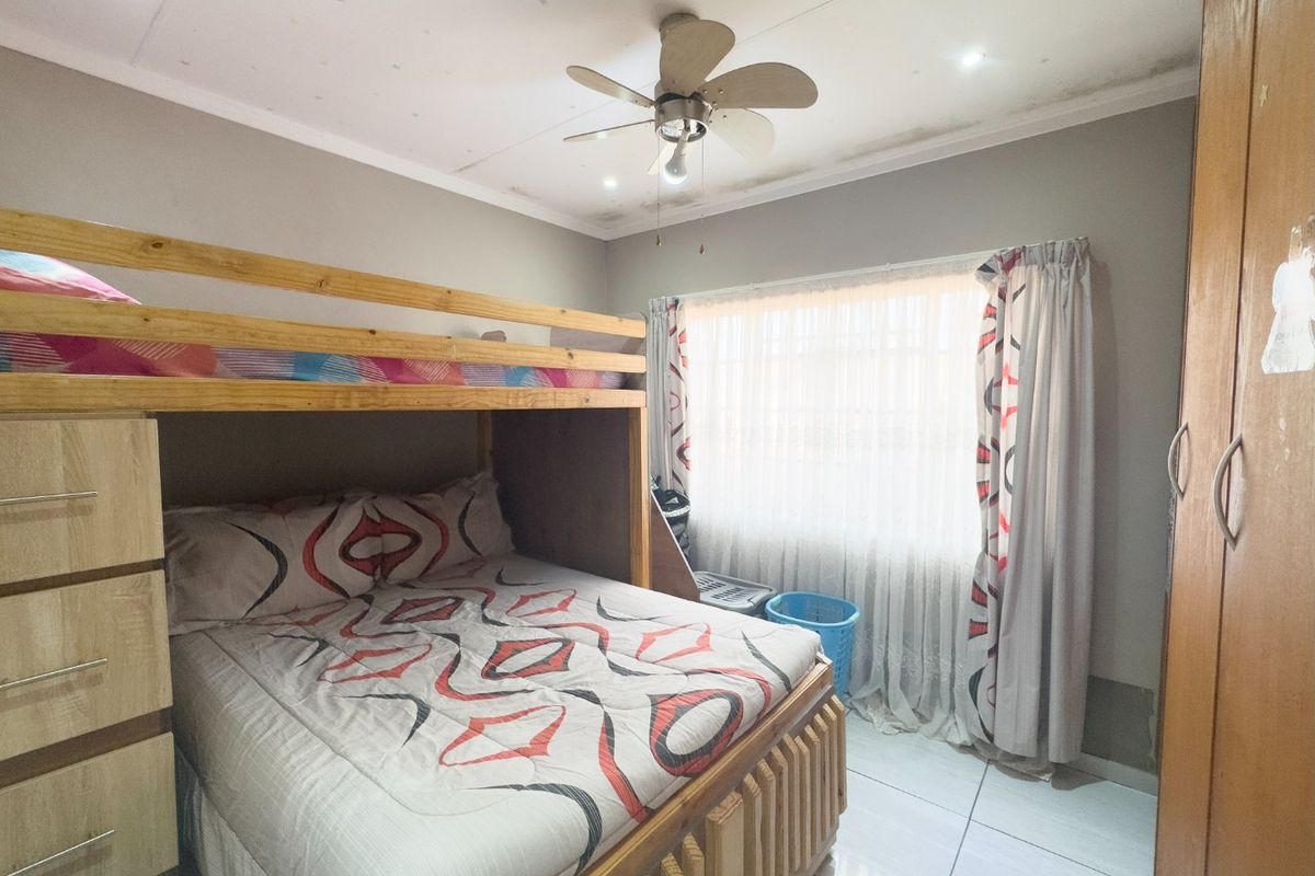 A bedroom featuring tiled flooring, a ceiling fan, and a built-in wardrobe, showing signs of ceiling water damage and wear.