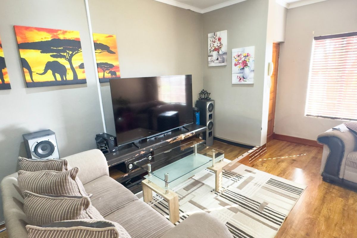 A comfortable living room featuring laminate flooring, neutral wall tones, and natural light filtered through venetian blinds.