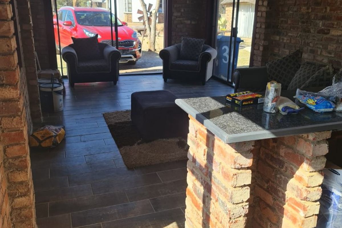 An open-plan living area featuring exposed brick walls, tiled flooring, a built-in brick bar counter with a stone top, and large sliding glass doors.