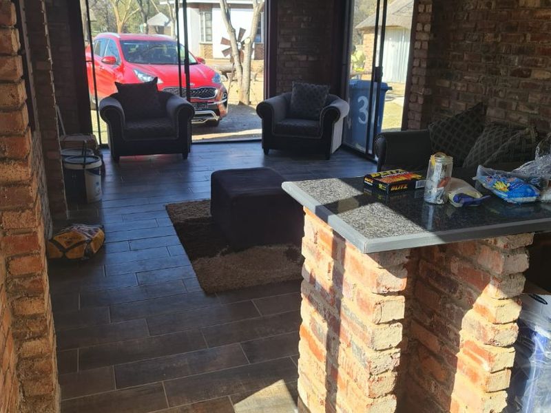 An open-plan living area featuring exposed brick walls, tiled flooring, a built-in brick bar counter with a stone top, and large sliding glass doors.