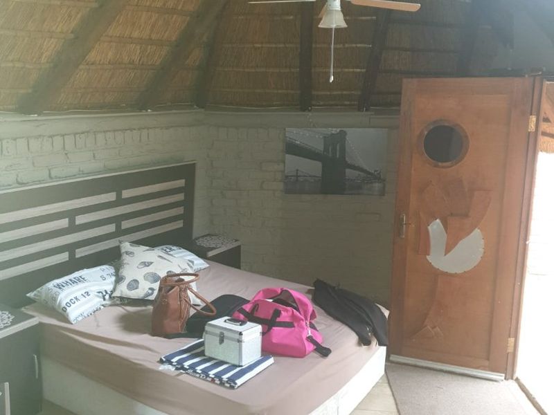 A bedroom featuring a high thatched roof, exposed brick walls, tiled flooring, and a ceiling fan.