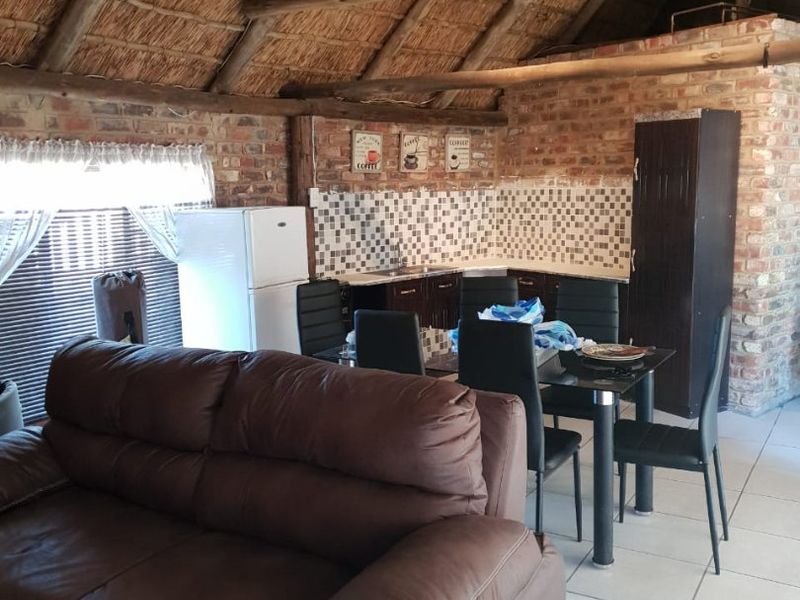 Open-plan living and kitchen area featuring a high vaulted thatched roof, exposed brick walls, and tiled flooring.