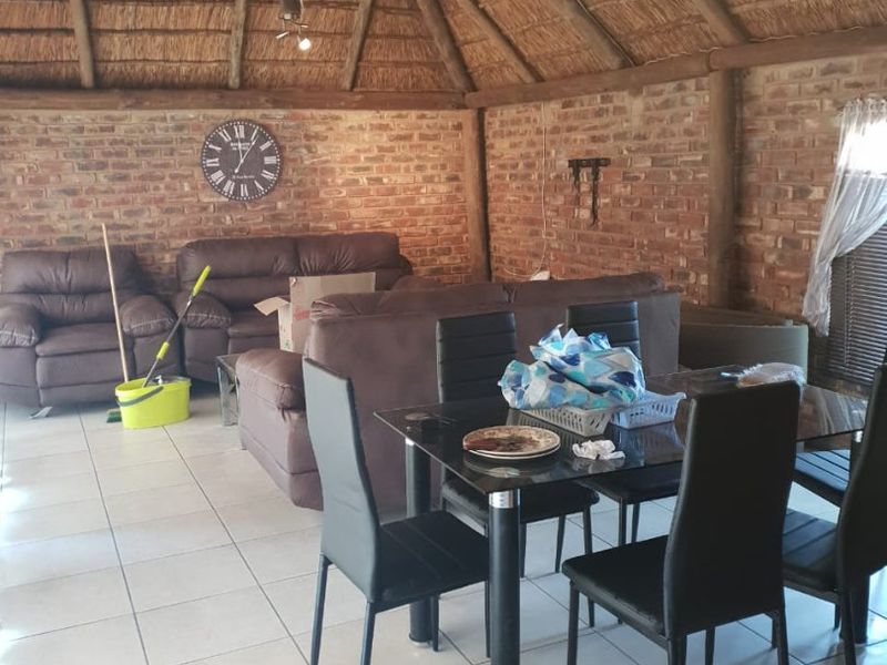 Open plan living and dining area featuring a high vaulted thatch ceiling, exposed brick walls, and tiled flooring.
