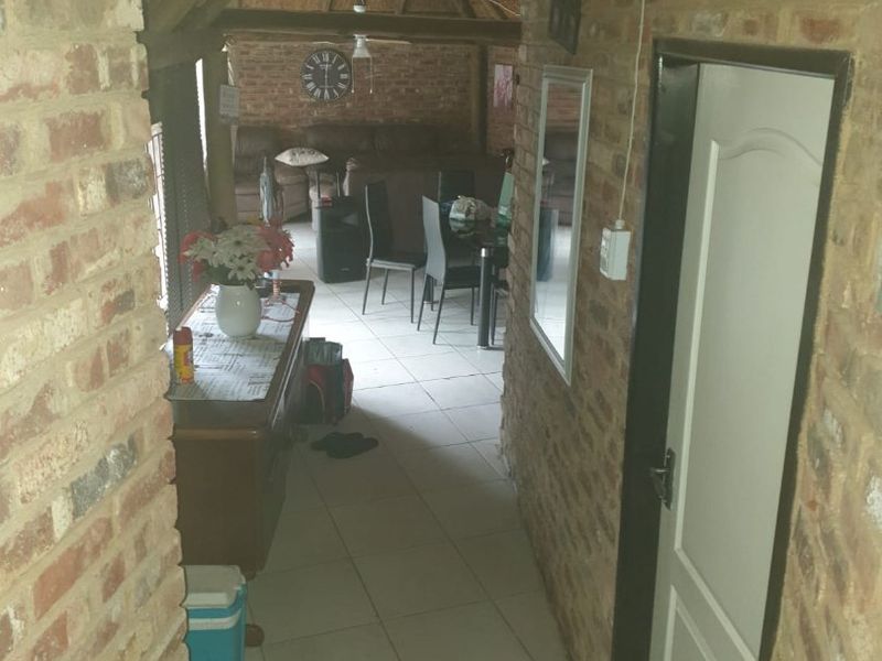 A view through a hallway into an open plan living and dining area featuring exposed brick walls and a traditional thatched roof structure.