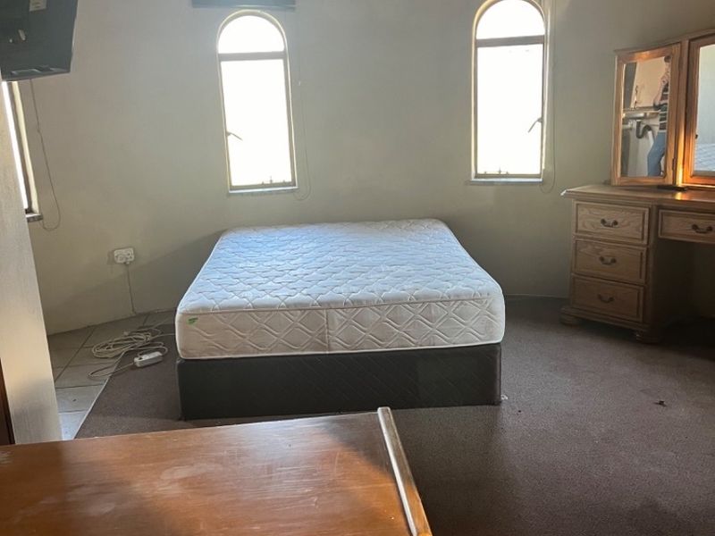 Spacious bedroom featuring a unique thatched roof ceiling, arched windows, and carpeted flooring, offering a rustic architectural aesthetic.