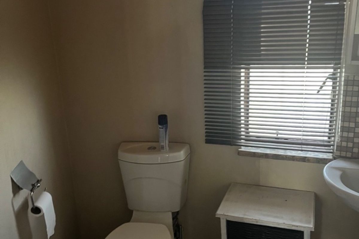 A compact bathroom featuring a standard toilet, pedestal basin, and tiled flooring, illuminated by an arched window with fitted venetian blinds.