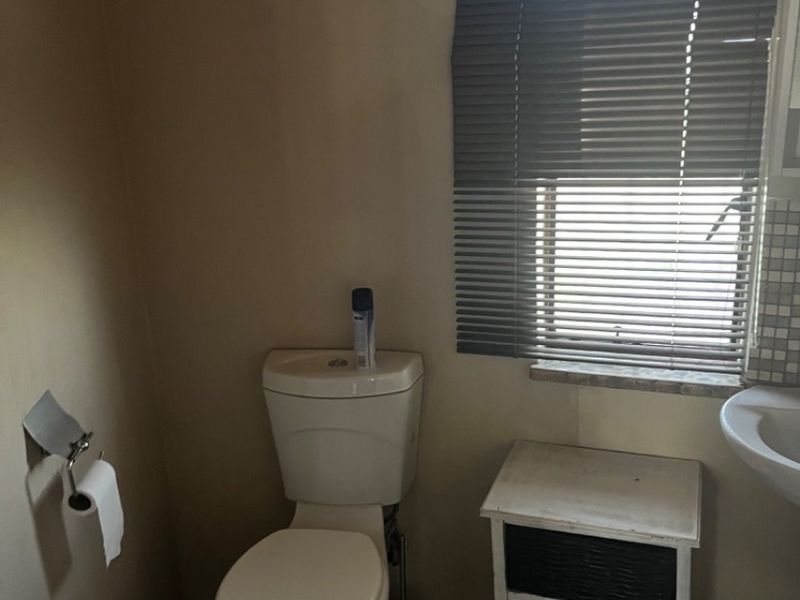 A compact bathroom featuring a standard toilet, pedestal basin, and tiled flooring, illuminated by an arched window with fitted venetian blinds.