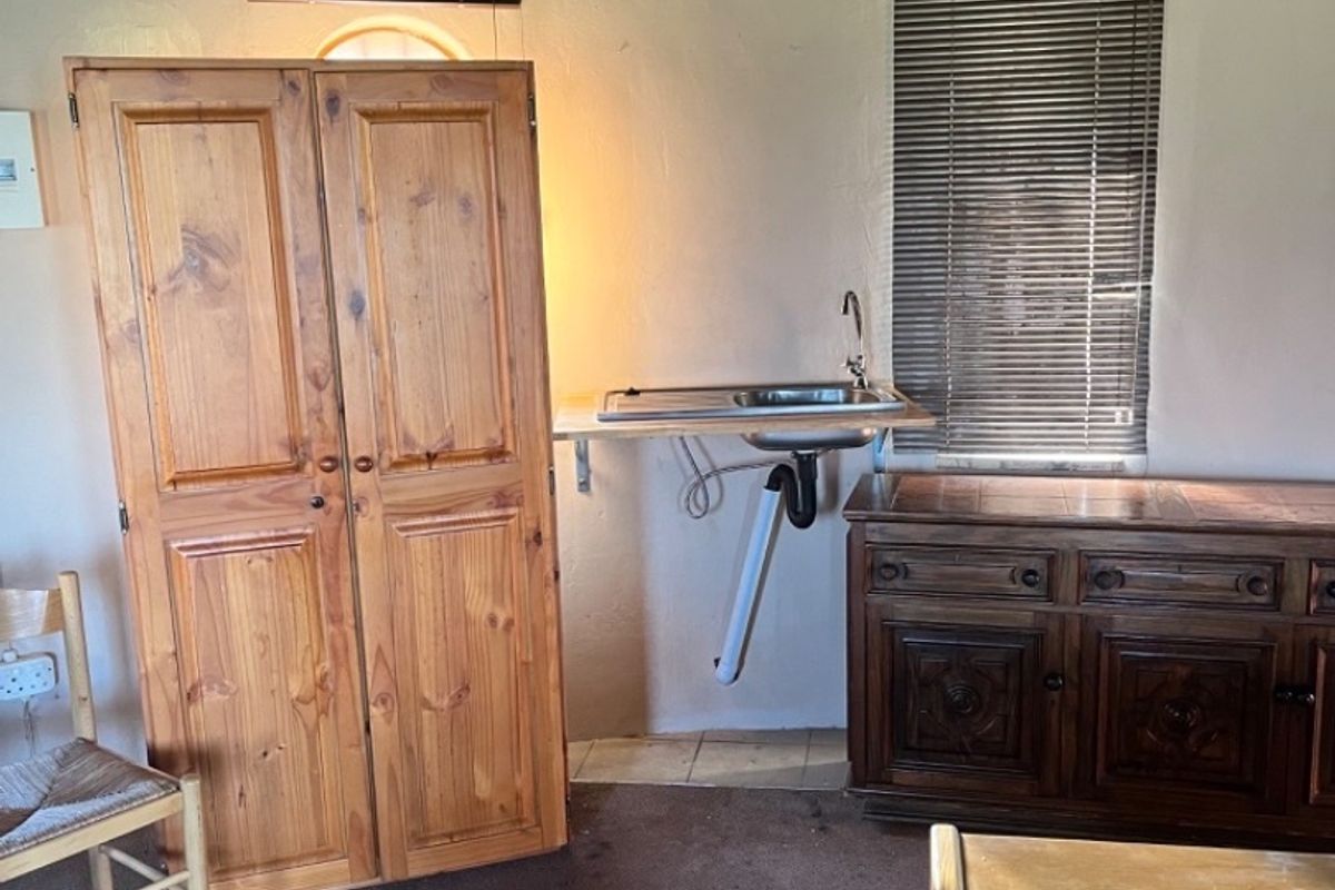 A small kitchenette area featuring a stainless steel sink, exposed plumbing, and a traditional thatch ceiling in a dated interior space.