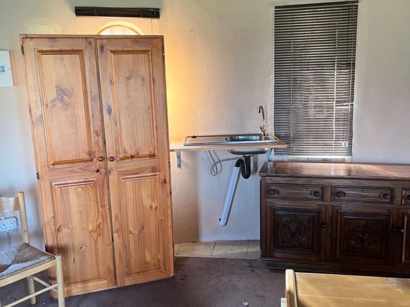 A small kitchenette area featuring a stainless steel sink, exposed plumbing, and a traditional thatch ceiling in a dated interior space.