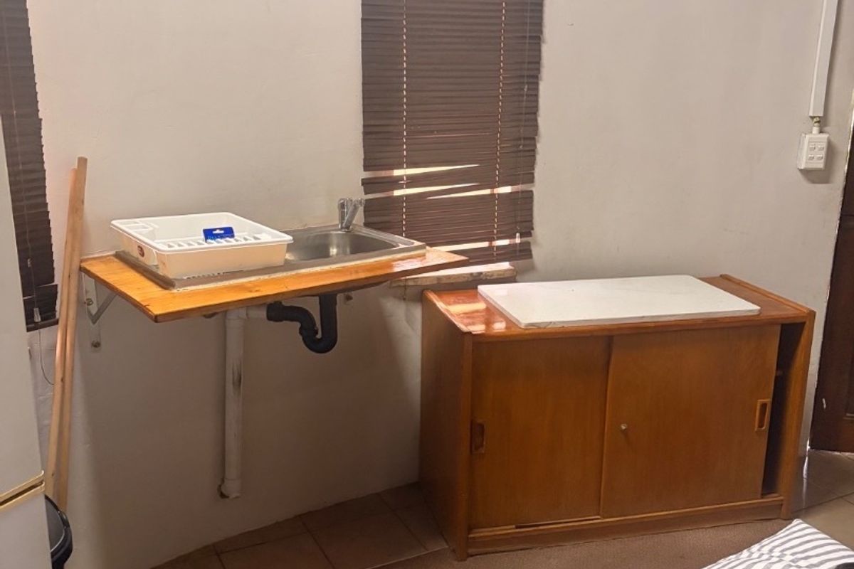 A functional scullery or utility area featuring a wall-mounted stainless steel sink, exposed plumbing, and a built-in wooden storage cabinet.