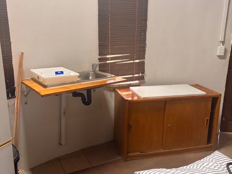 A functional scullery or utility area featuring a wall-mounted stainless steel sink, exposed plumbing, and a built-in wooden storage cabinet.