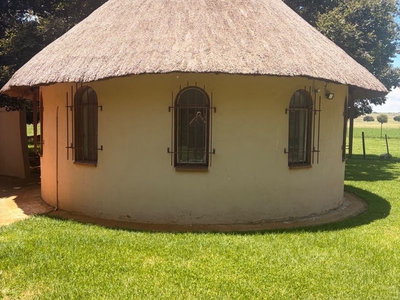 A charming circular structure featuring a traditional thatched roof and arched windows with security bars, set within a well-maintained garden area.