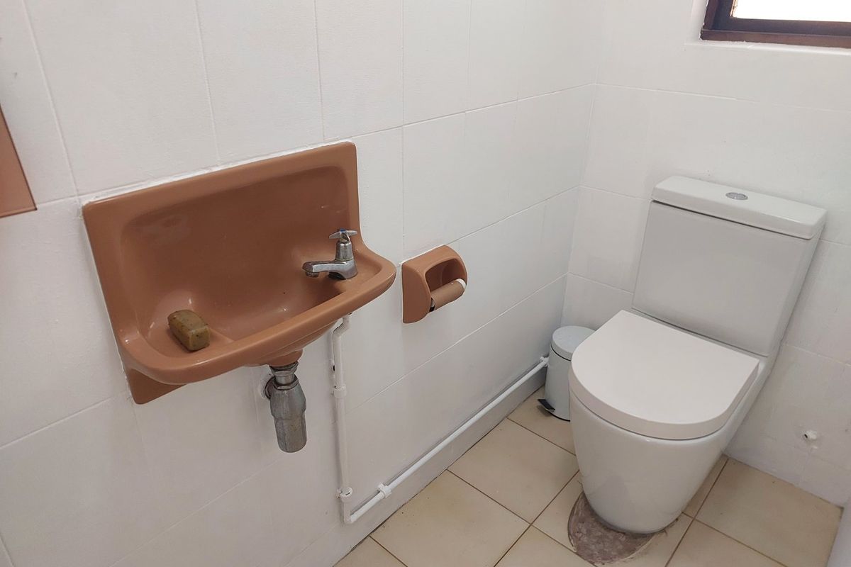 A compact bathroom featuring a wall-mounted basin, a standard toilet, and tiled finishes. The space is functional but would benefit from modern updates.