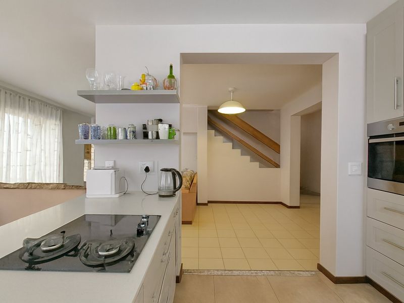 Open plan kitchen area featuring modern cabinetry, built-in oven, electric hob, and stone countertops, flowing into a tiled living space with a staircase.