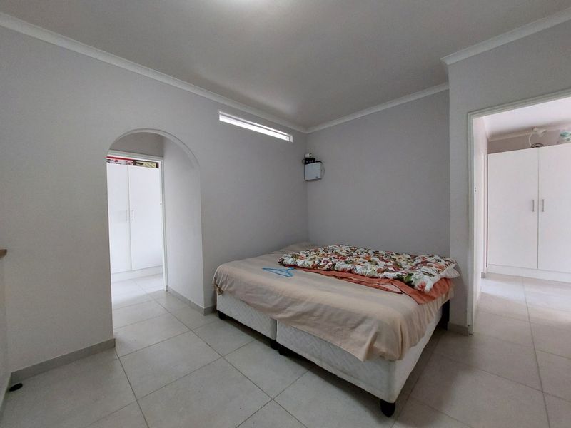 A bedroom featuring tiled flooring, an arched doorway, and built-in cupboards, providing a functional and neutral living space.