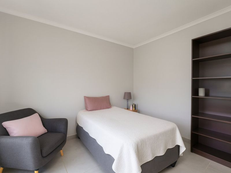 A clean and well-maintained bedroom featuring neutral wall tones, tiled flooring, and a built-in shelving unit.