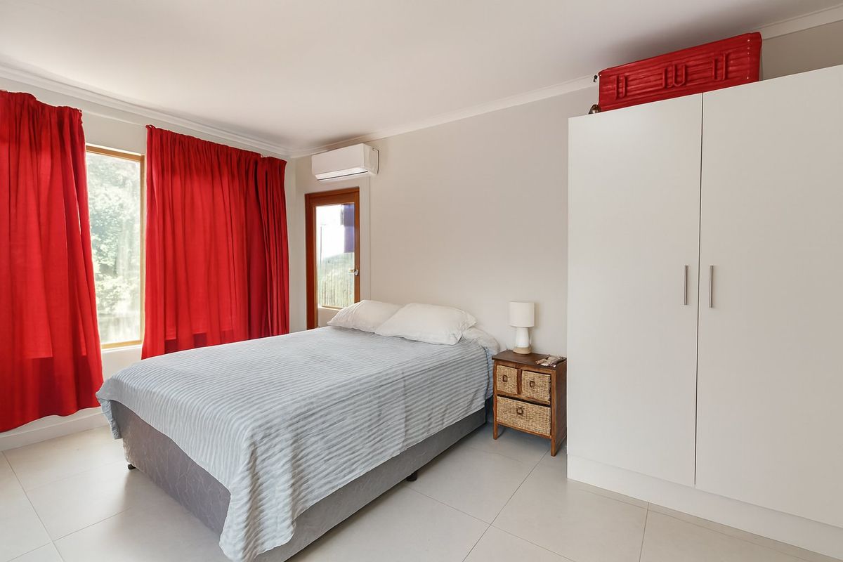 A bright bedroom featuring tiled flooring, a built-in wardrobe, and a wall-mounted air conditioning unit with access to an outdoor area.
